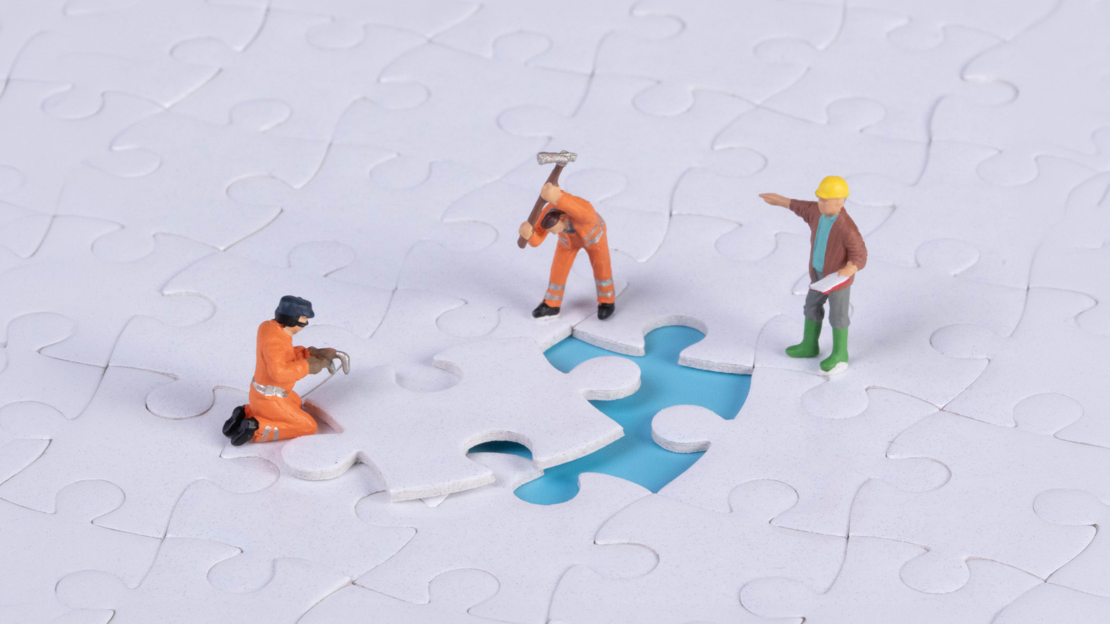 Miniature figures fitting the last piece into a jigsaw puzzle